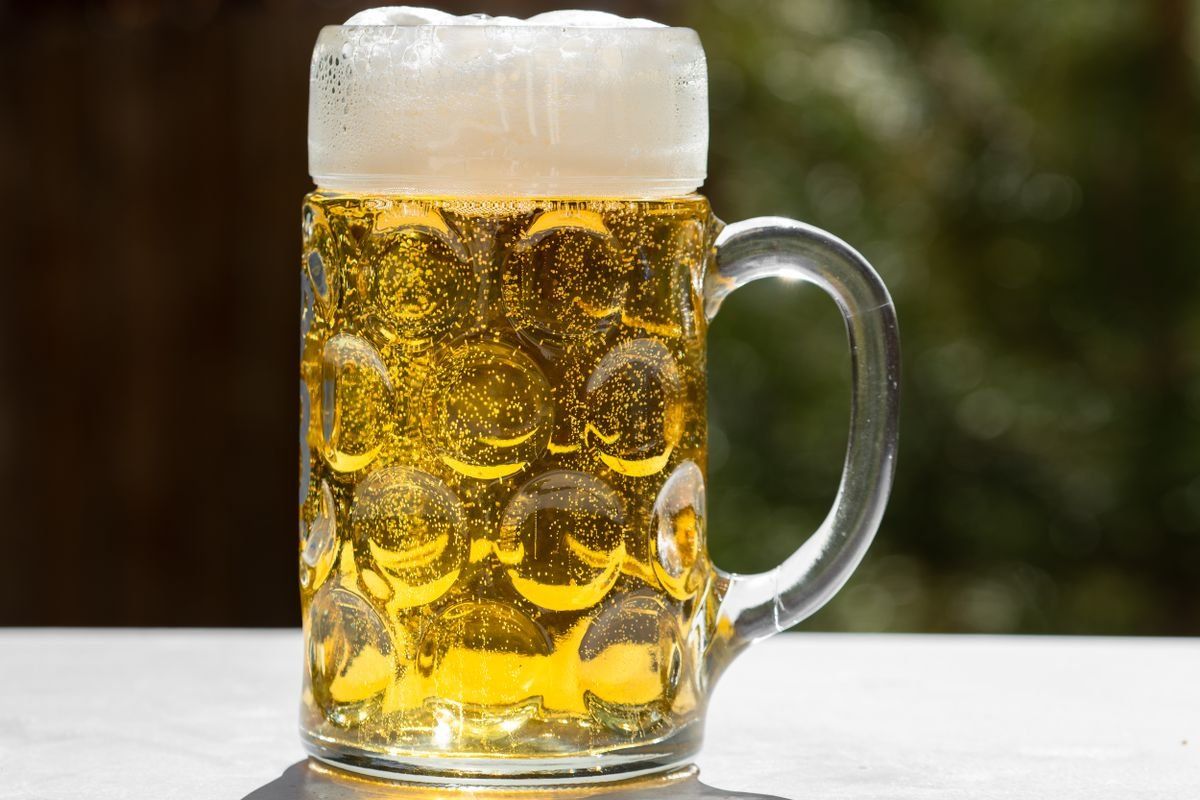 Glass mug of golden beer with a thick foamy head on an outdoor table