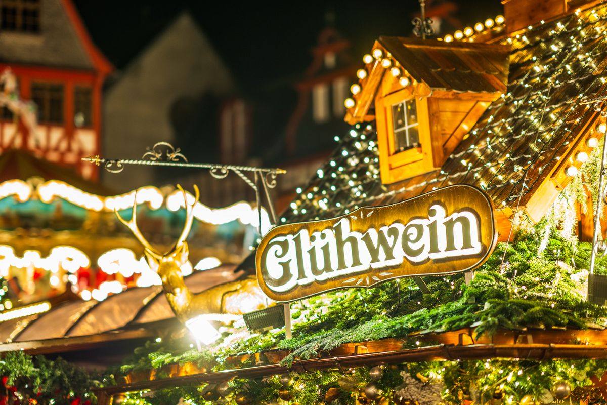 Glühwein sign on a decorated market stall roof with lights and greenery at night
