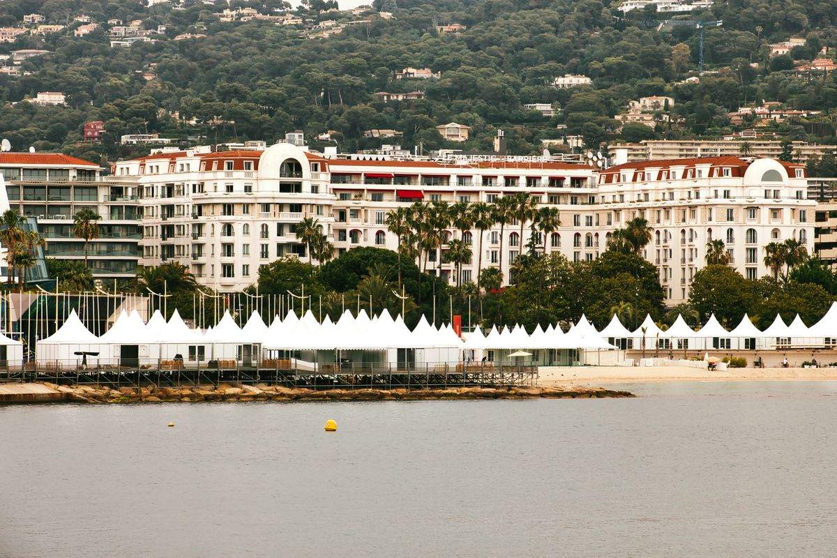 Grand white waterfront hotel with palm trees and beach tents in Cannes