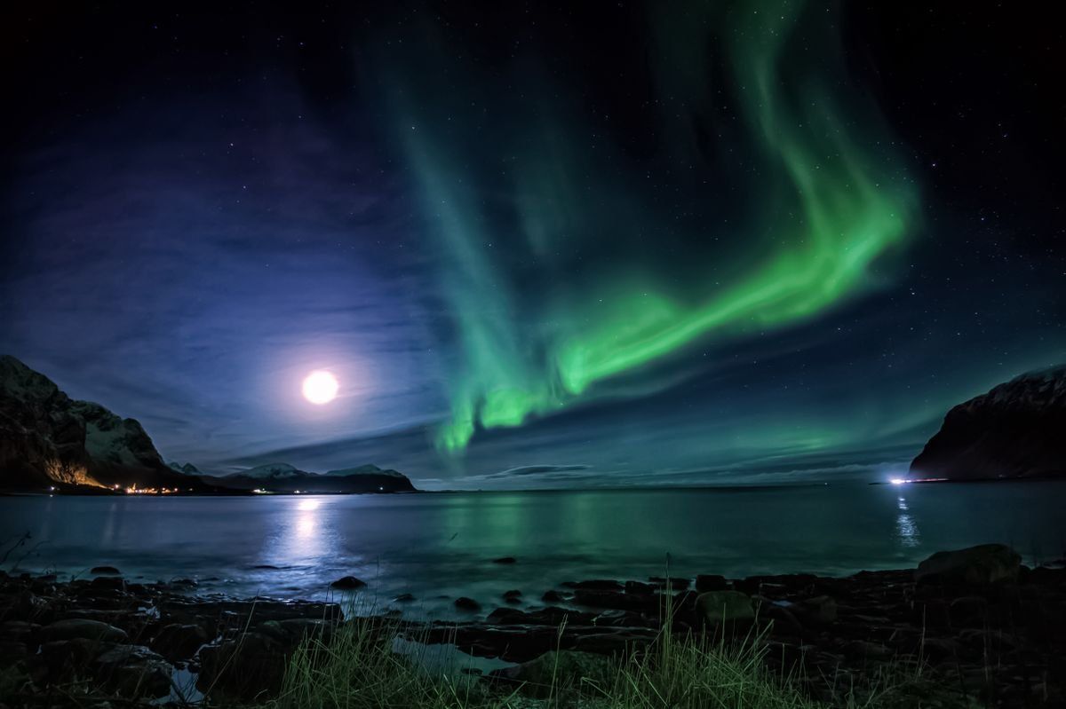 Green Northern Lights over a calm fjord with moonlight and dark mountain silhouettes