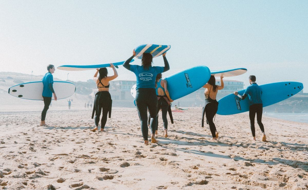 Group of surfers carrying blue boards across a sunny sandy beach
