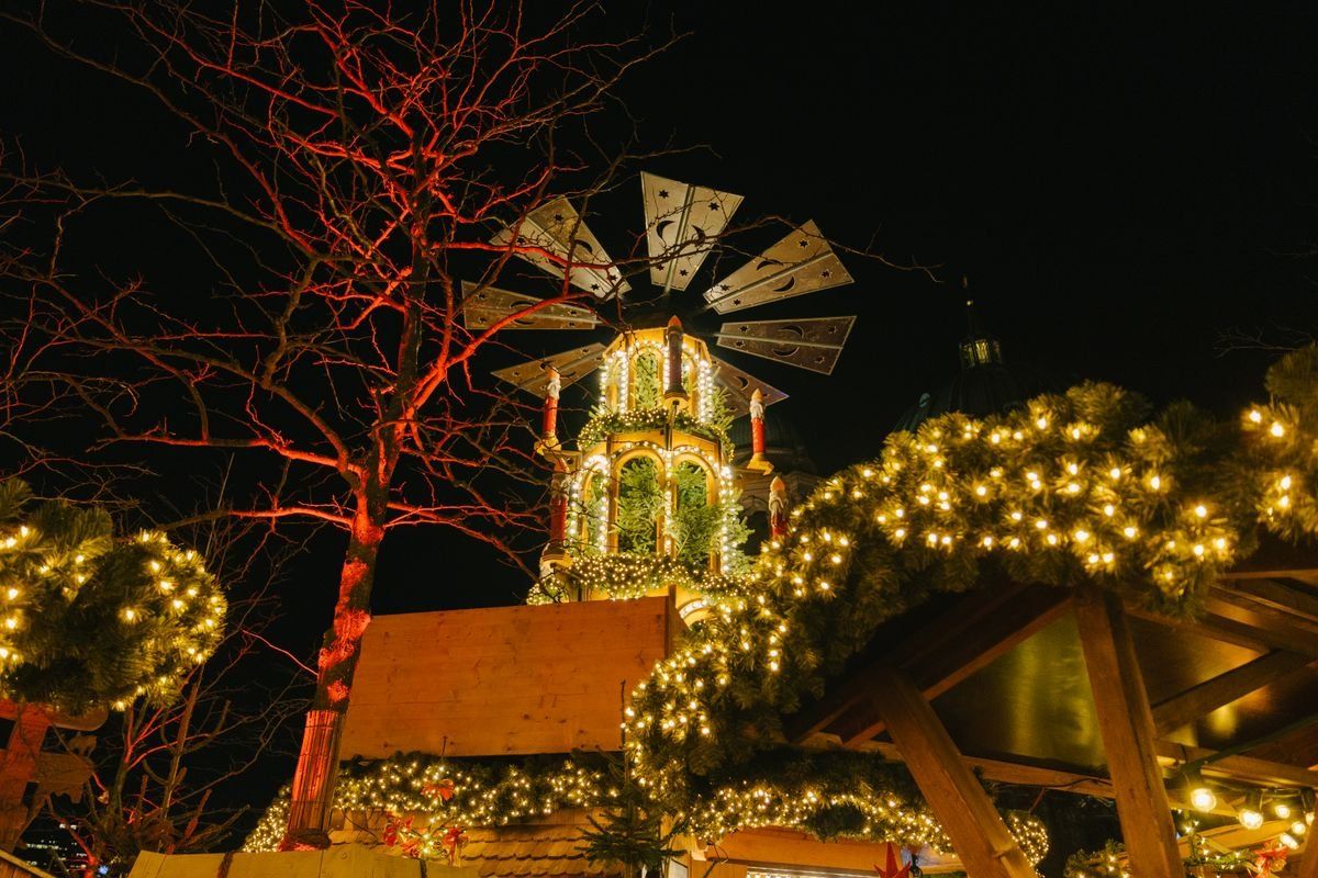 Illuminated Christmas market roofs and a traditional carousel tower under the night sky