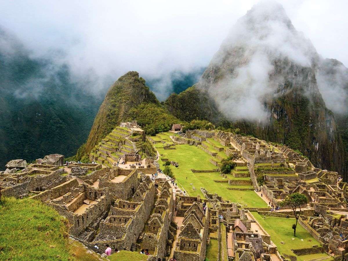 Machu Picchu stone ruins with green terraces and mist drifting around steep mountain peaks