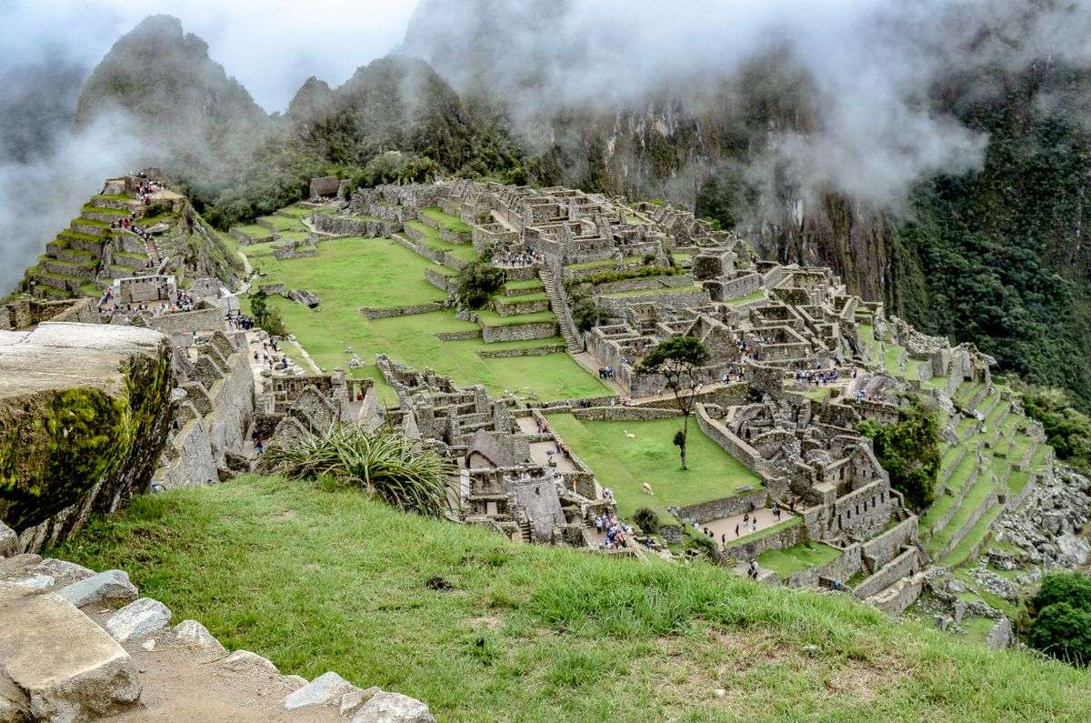 Machu Picchu terraces and stone structures on a green mountainside with fog rolling through the peaks