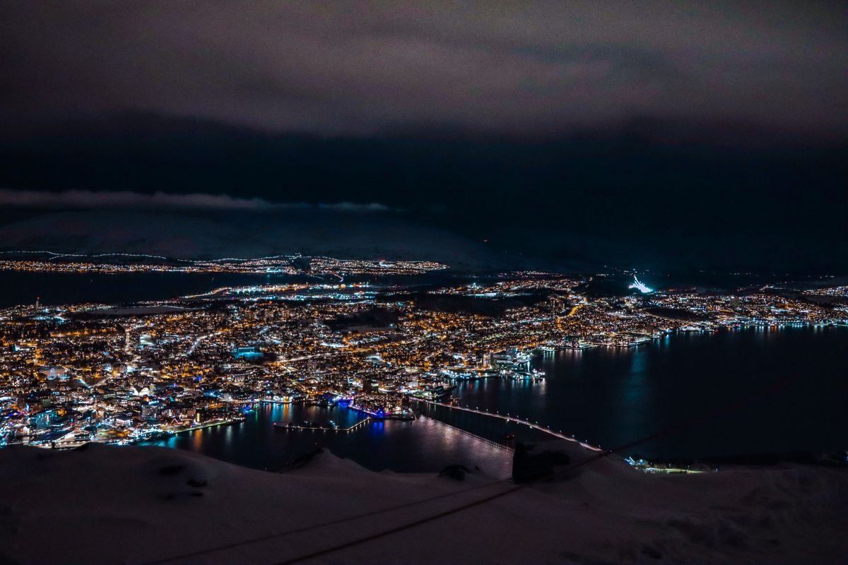 Night aerial view of Tromsø with glowing city lights, bridges and dark water
