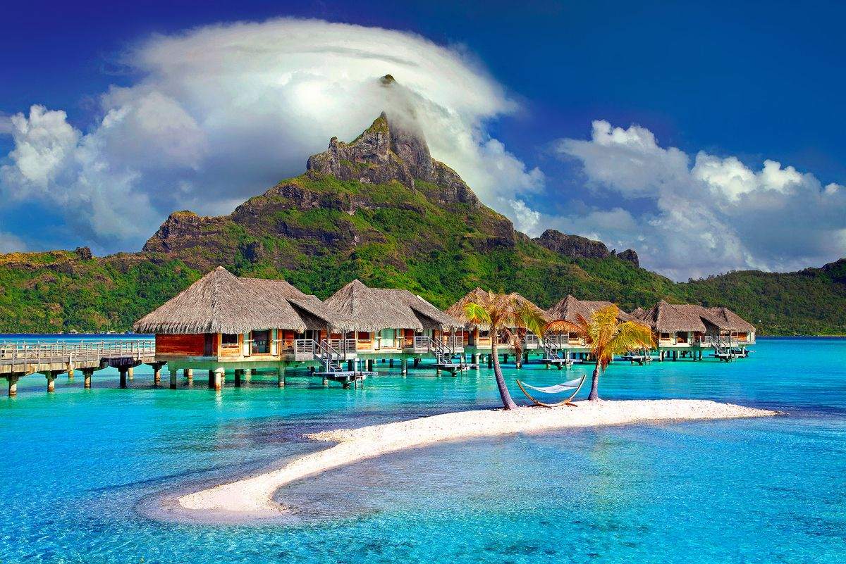 Overwater bungalows above turquoise lagoon with a steep green mountain in the background