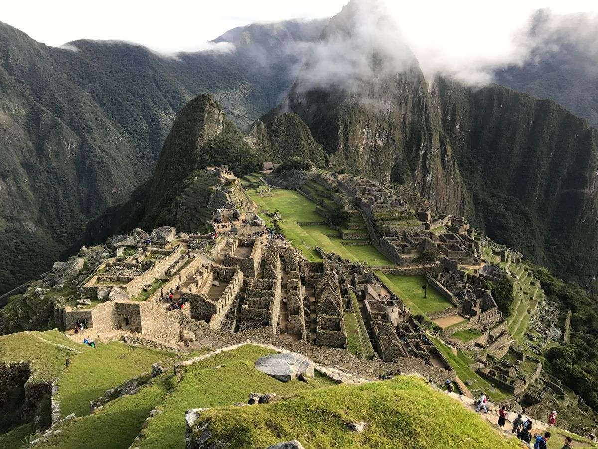 Panoramic view of Machu Picchu with terraced ruins, grassy slopes and clouds around the mountains