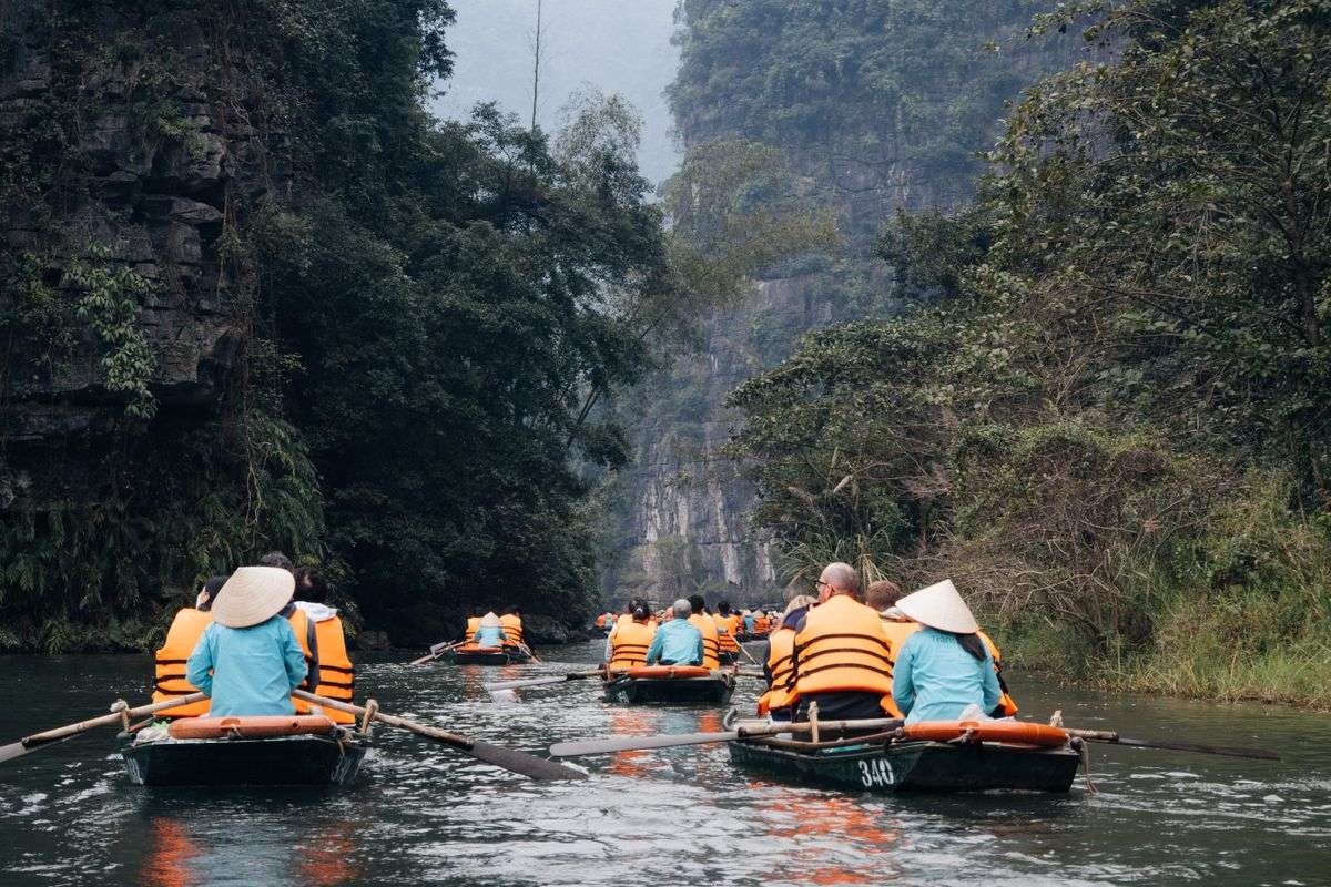 People in small boats wearing orange life jackets on a river between lush limestone cliffs