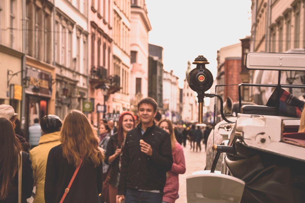 People walking along a narrow city street beside a historic carriage and old buildings