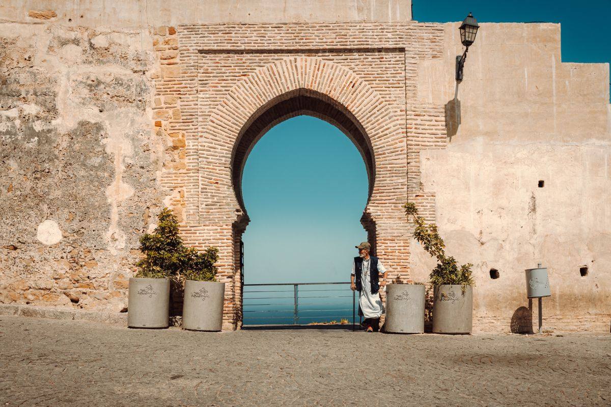 Person standing beside a historic stone archway with the sea visible through the opening