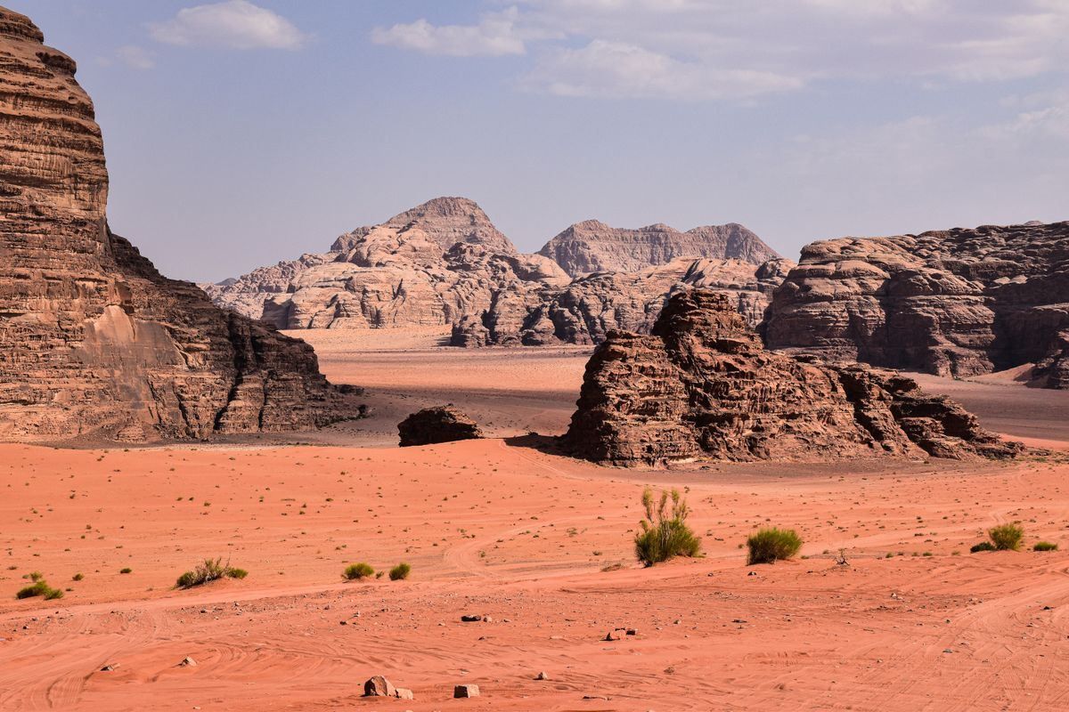 Rock formations and sandy desert plain in Wadi Rum under a light blue sky