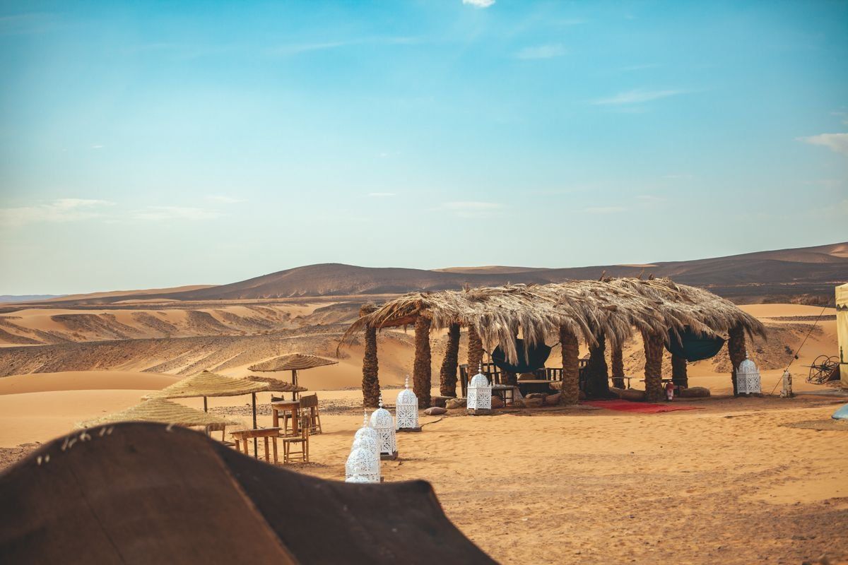 Rustic thatched shelter on sandy ground with desert dunes stretching into the distance