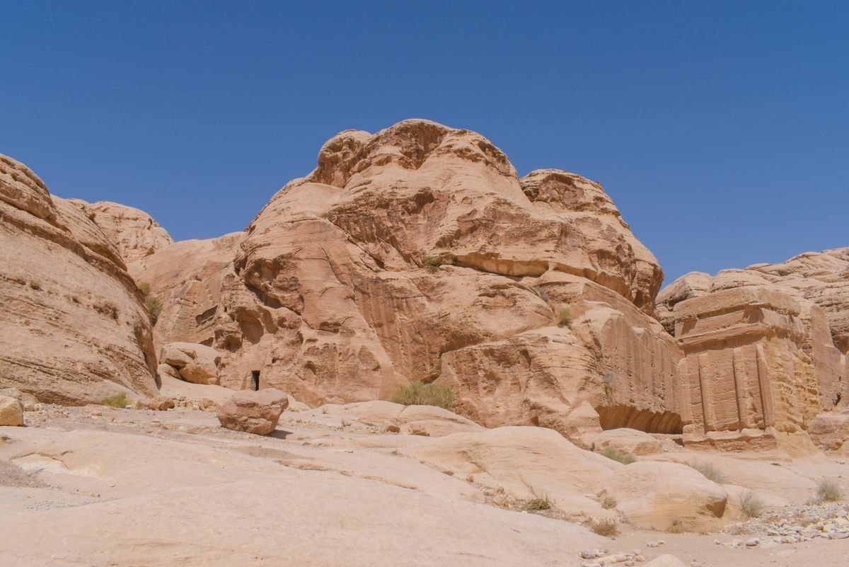 Sandstone rock formation with a carved facade on the right under a clear blue sky