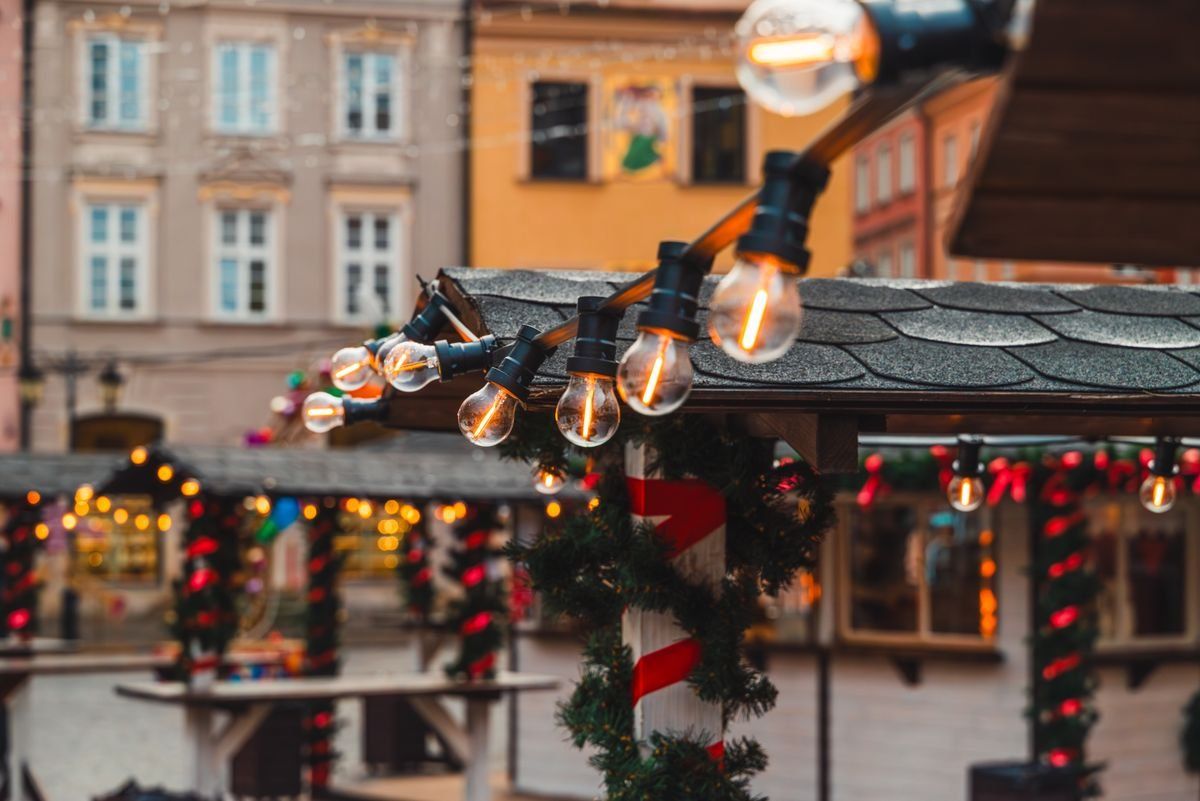 String lights over decorated wooden market stalls in an old town square