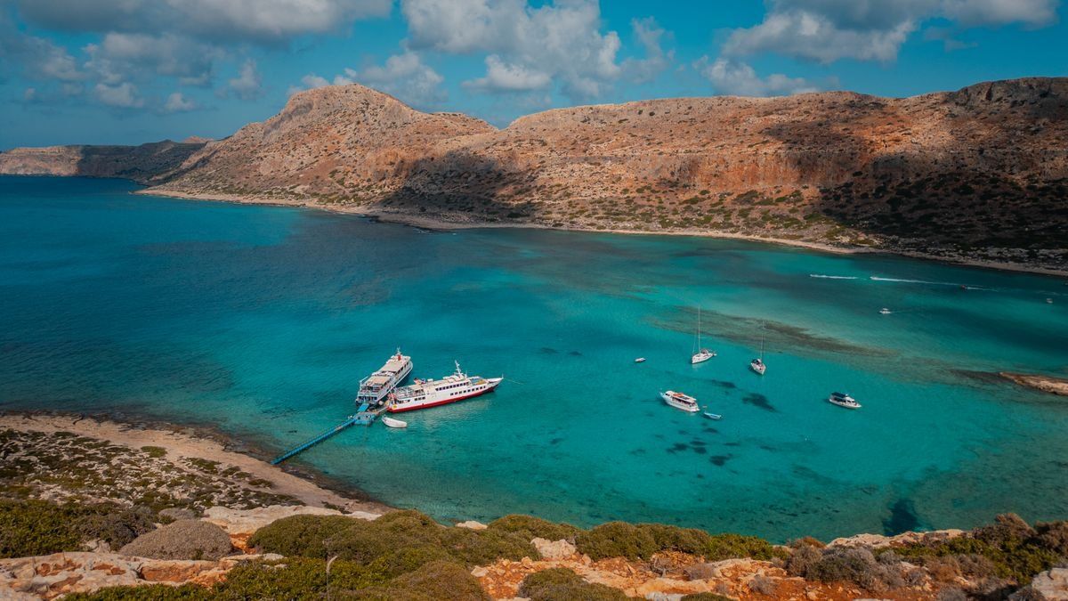 Turquoise lagoon at Balos Beach with anchored boats and dry hills beyond