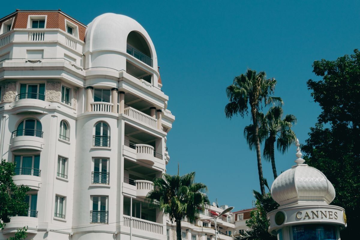 White curved building with palm trees and a Cannes sign under clear sky