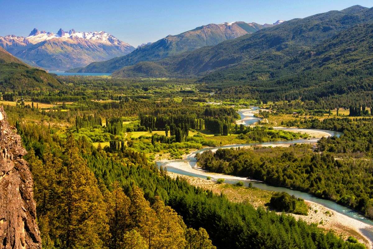 Winding river through a green valley with forested slopes and distant Andes peaks