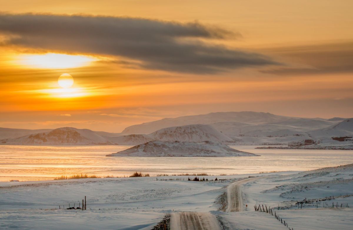 Winter sunset over snowy coastal hills and a winding road beside calm water