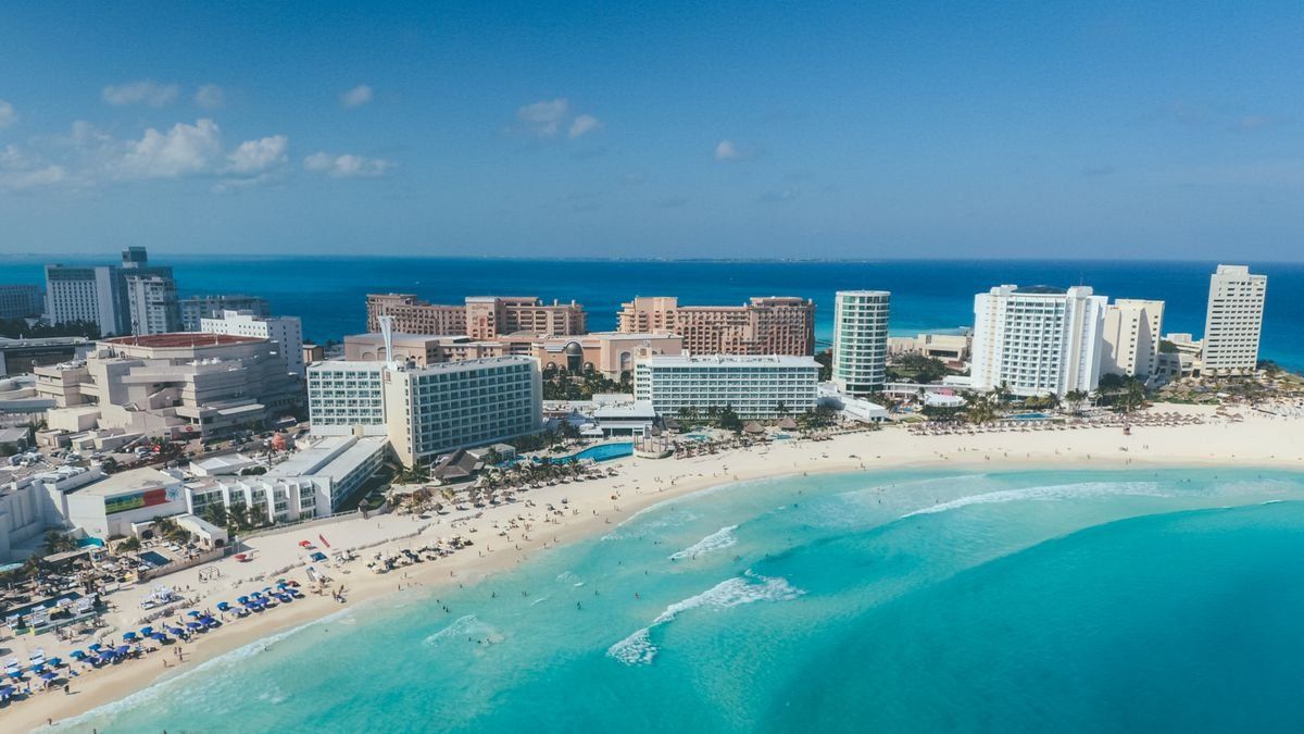 Aerial view of beachfront hotels and turquoise water along a wide sandy beach in Cancun