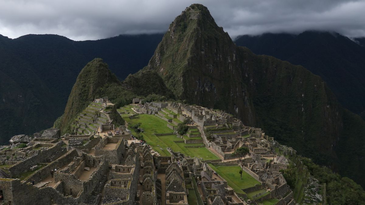 Aerial view of Machu Picchu stone ruins and green terraces below steep dark mountains
