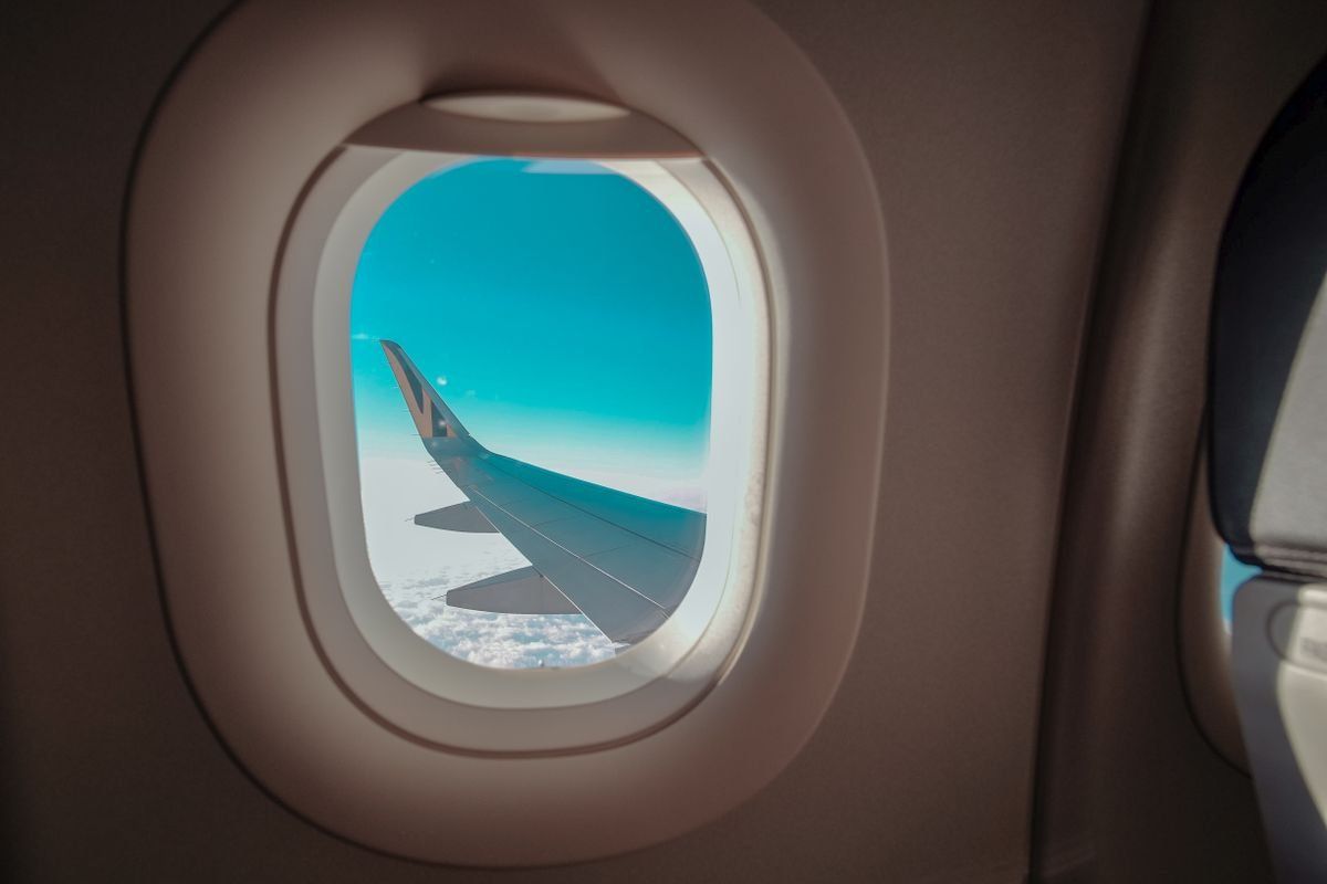 Airplane wing seen through a cabin window against a bright blue sky
