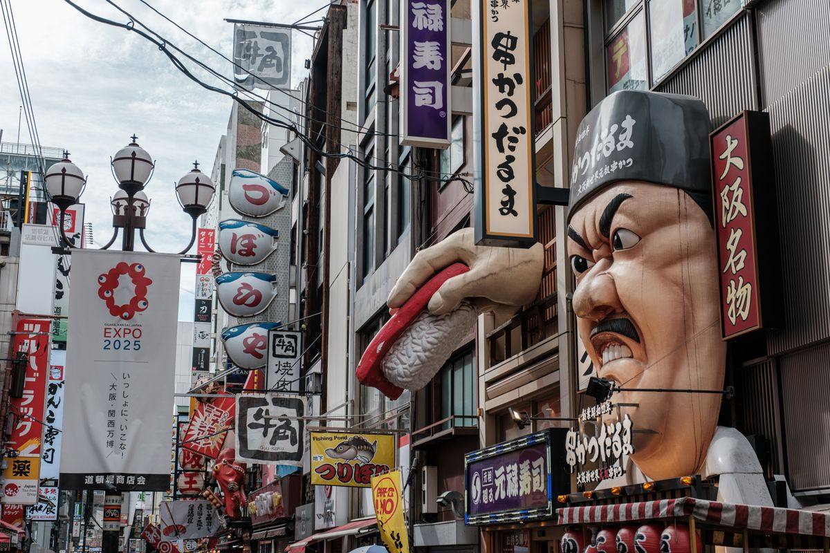 Busy Osaka street with vertical signs, a giant chef head and a hand holding sushi