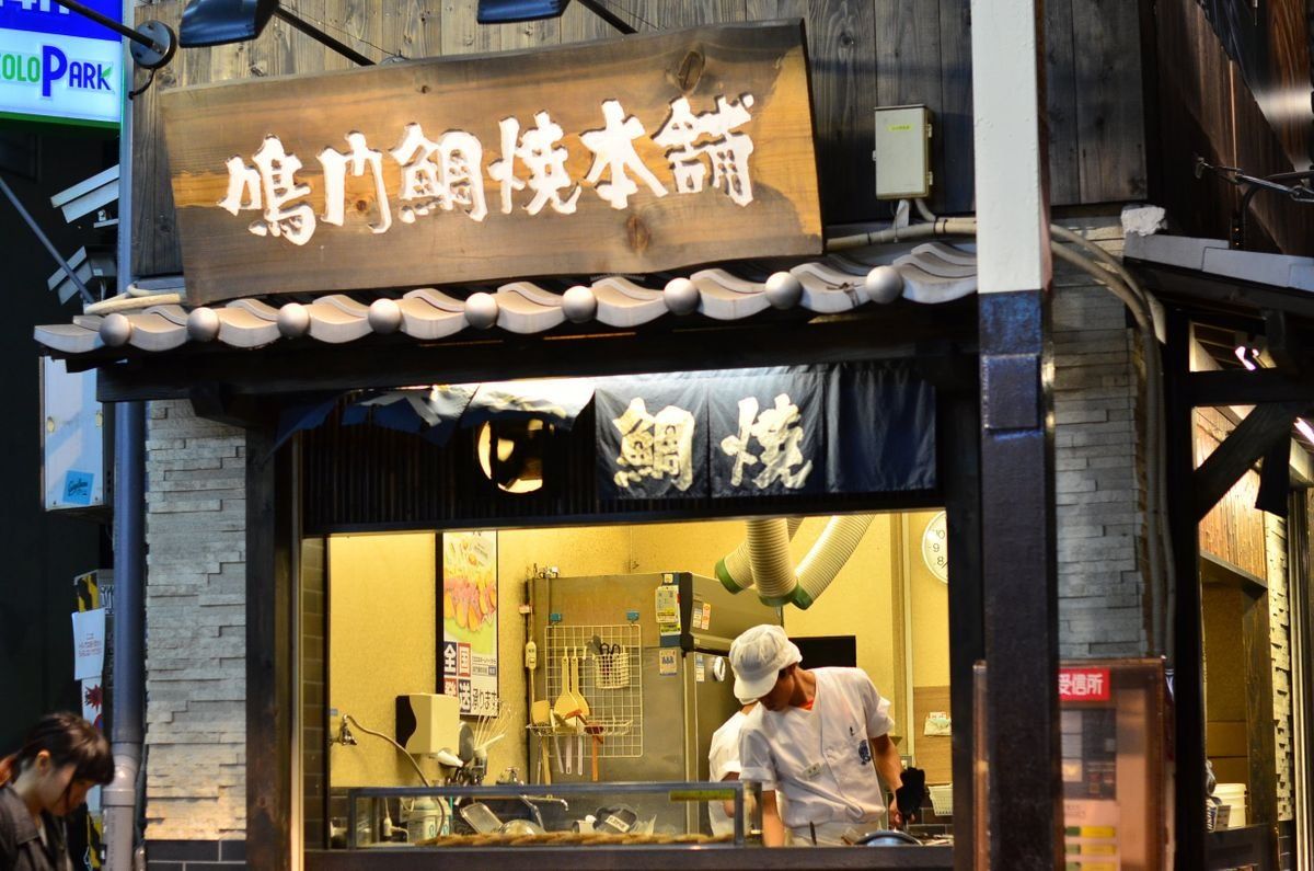 Cook working inside a small street food stall with glowing signs and wooden facade