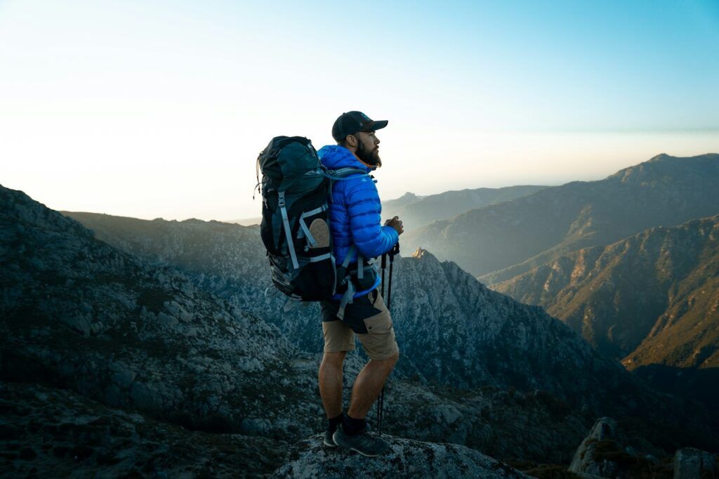 Hiker with a backpack standing on a rocky ridge overlooking a mountain valley