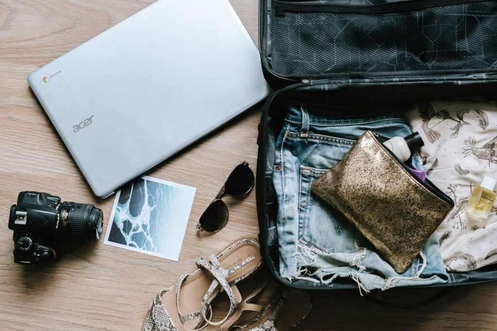 Camera, sunglasses, laptop and an open suitcase ready for a trip