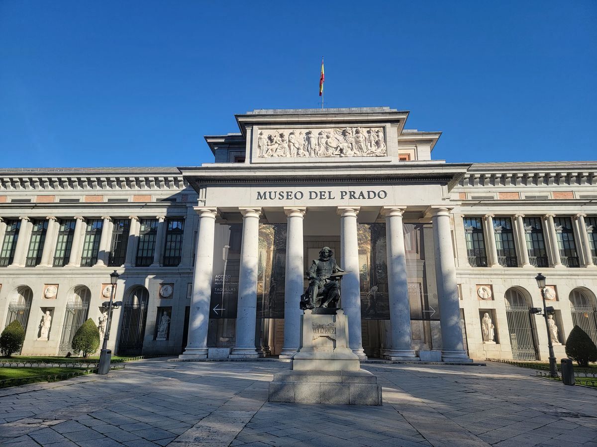 Front facade of Museo del Prado with columns and statue under a blue sky