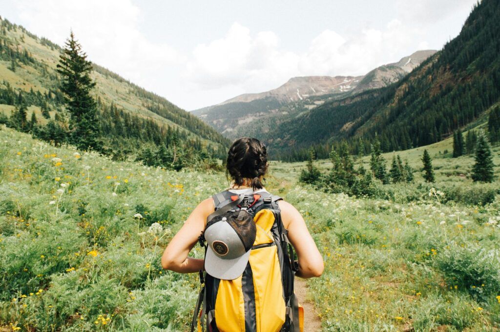 Person with a yellow backpack walking through a green mountain valley
