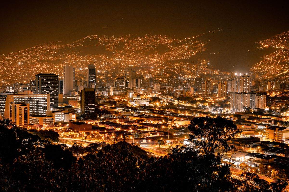 Medellín skyline at night with glowing buildings and hillside lights across the valley