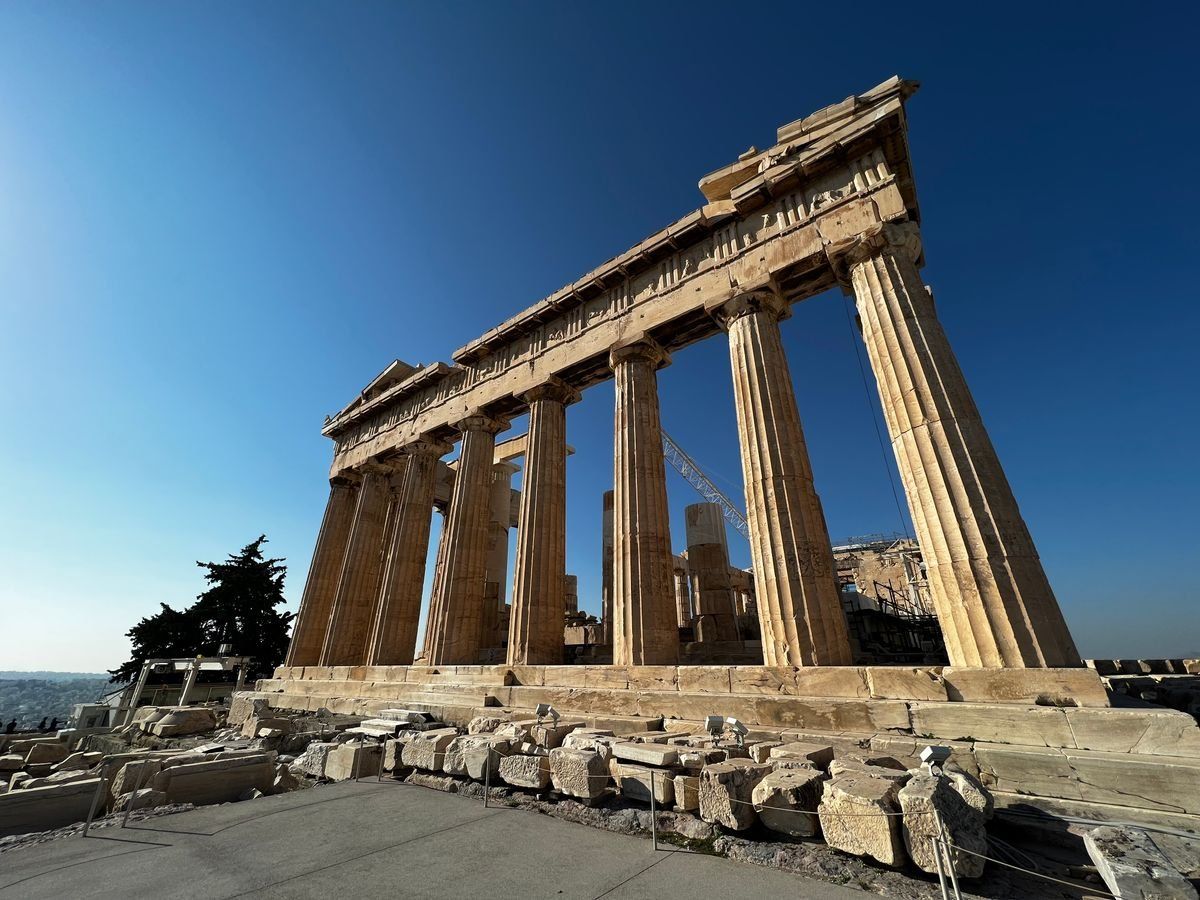The Parthenon ruins with tall stone columns and scattered marble blocks beneath a clear blue sky