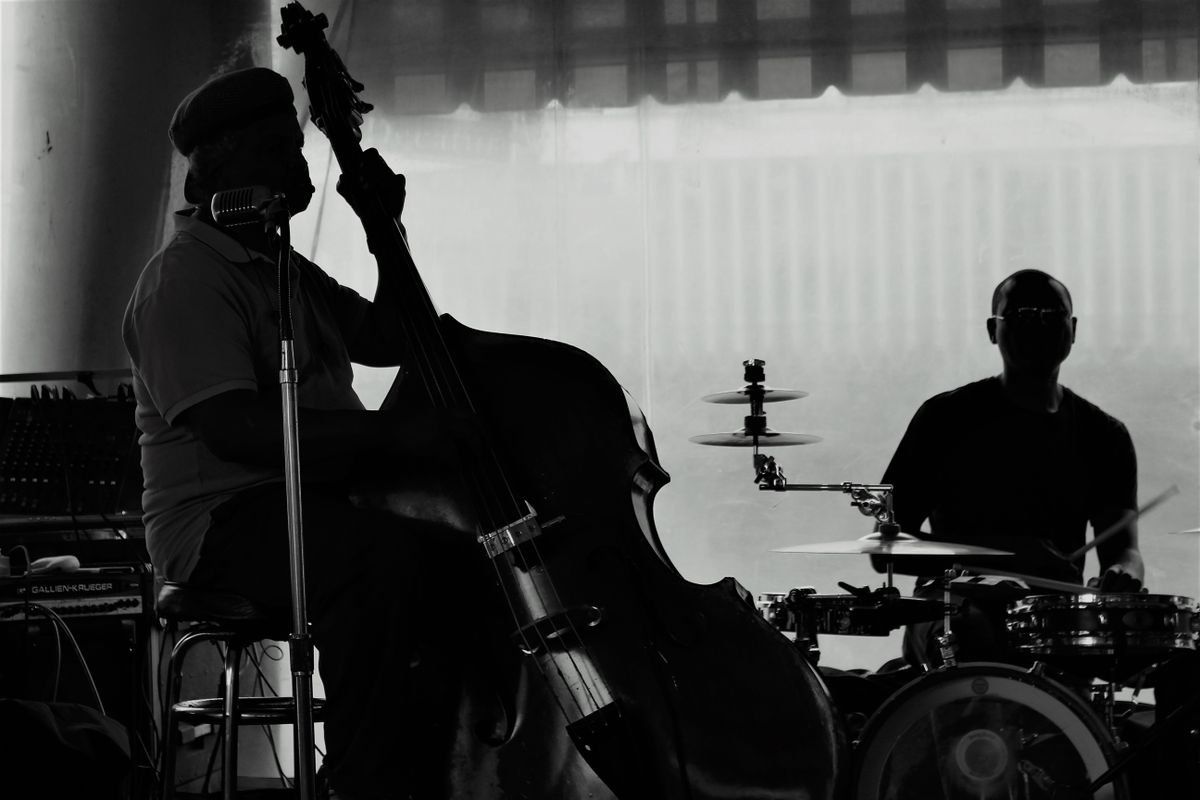 Silhouetted double bass player and drummer performing on a dimly lit stage