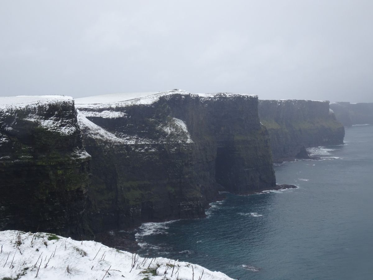 Snow-covered Cliffs of Moher above a grey sea under an overcast sky