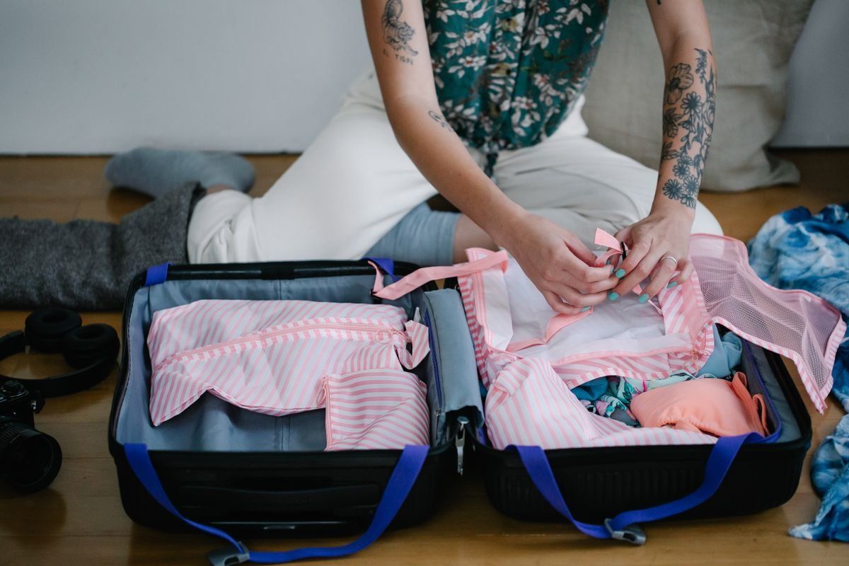 Woman kneeling on the floor and packing clothes into an open suitcase