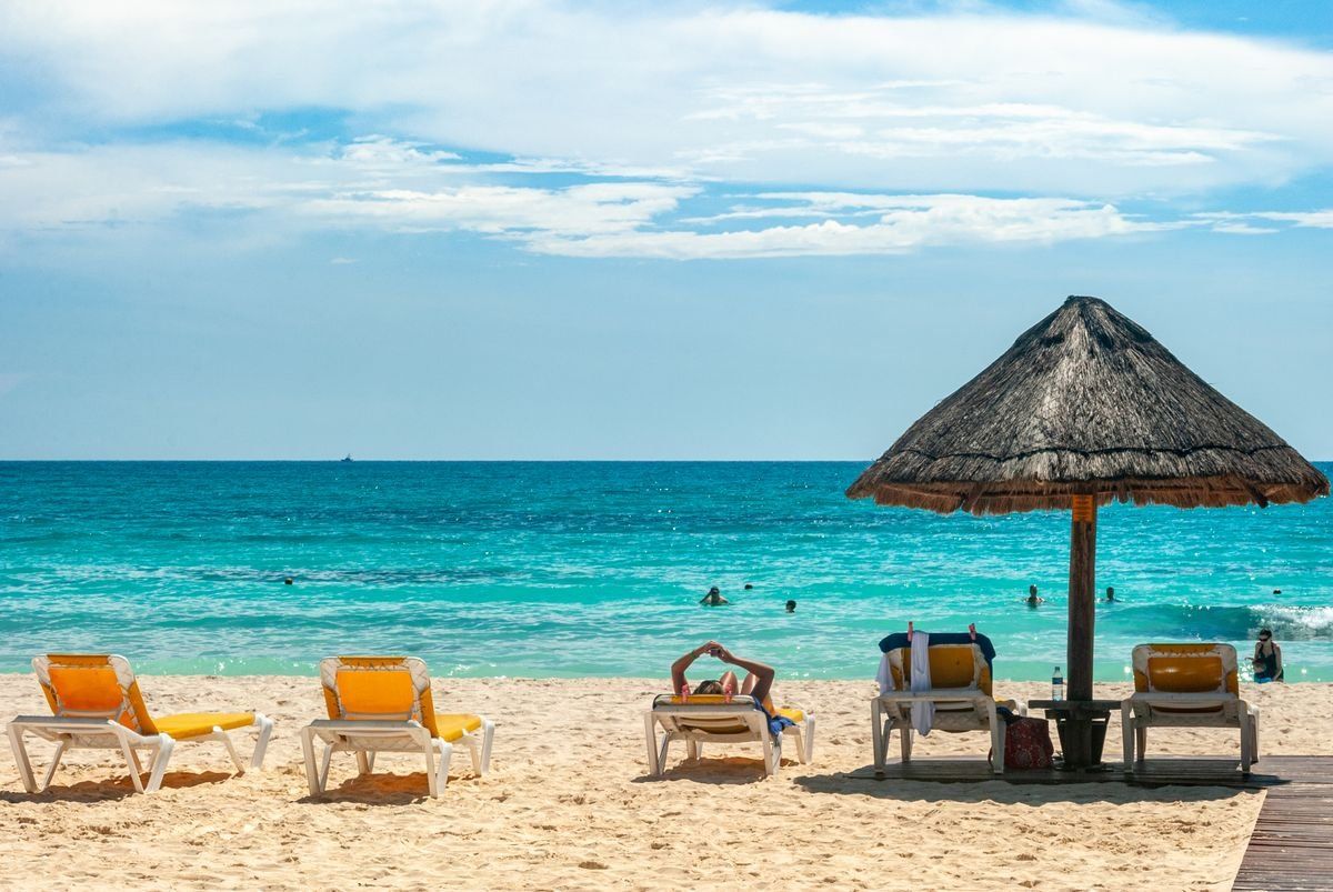 Yellow lounge chairs and a thatched umbrella on a sandy beach by clear blue water in Cancun
