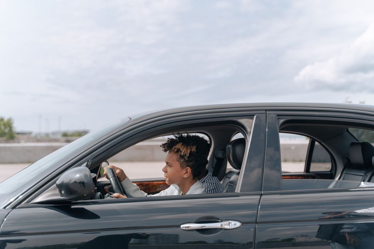 Young man driving a black car in daylight, seen from the side